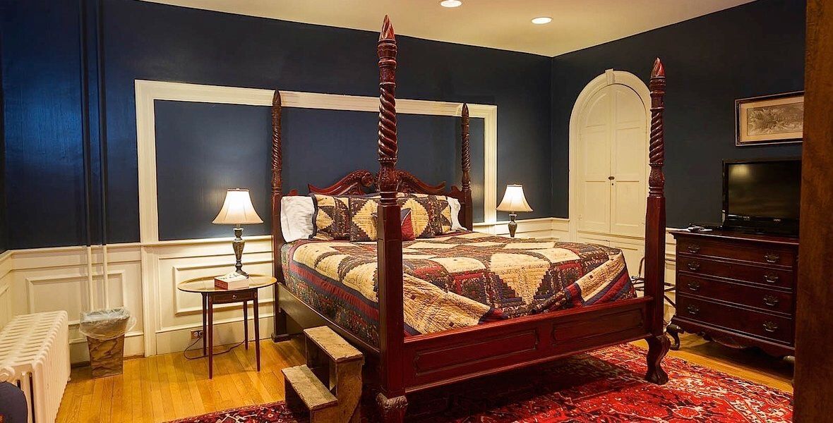 Elegant bedroom with a four-poster bed, dark blue walls, red rug, and matching wooden furniture