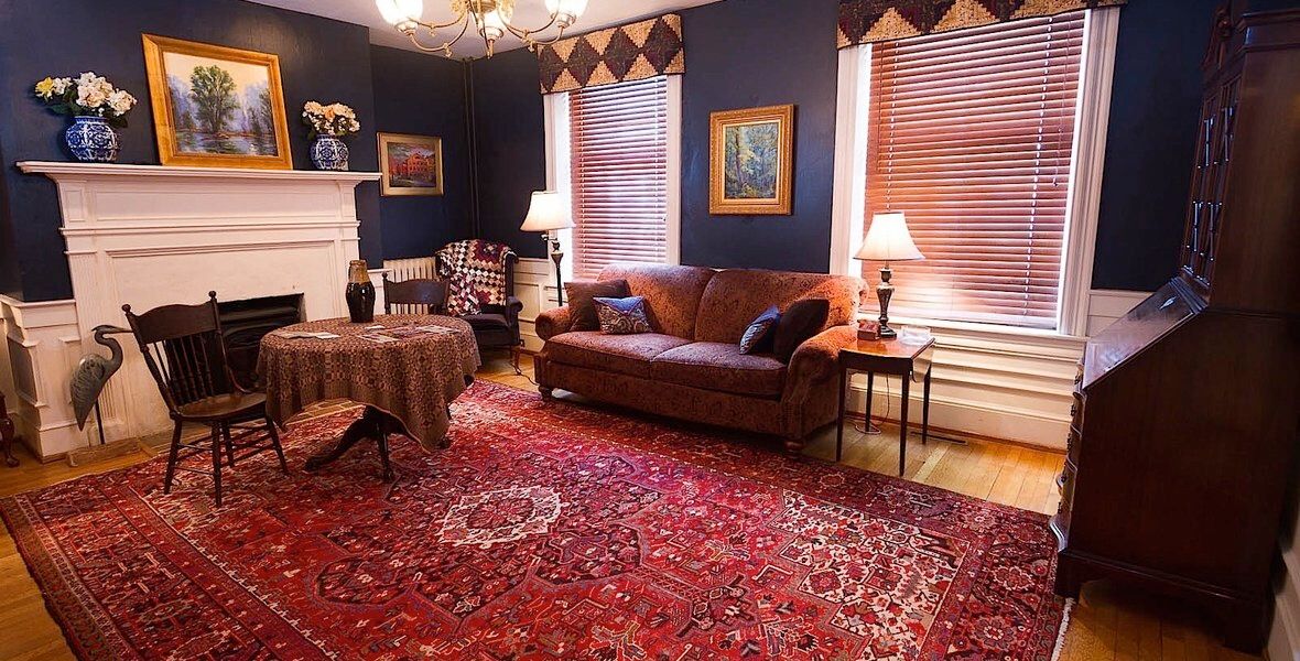 Cozy living room with red rug, brown sofa, fireplace, striped window shades, and framed wall art