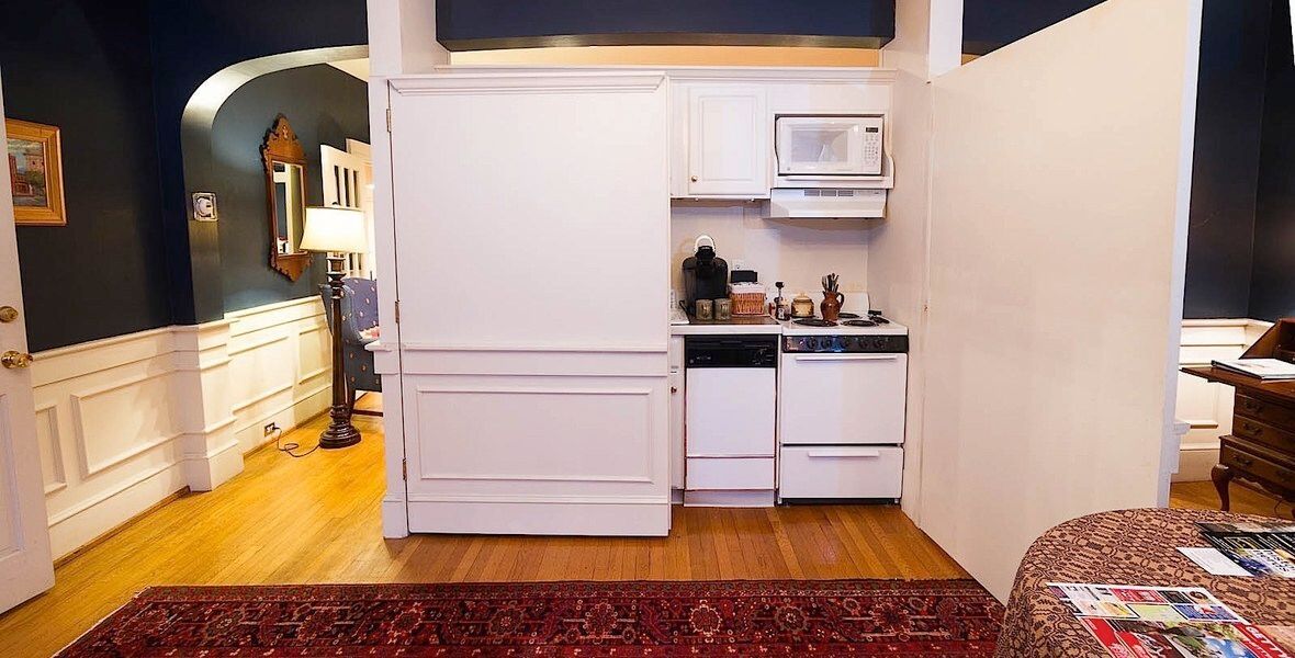 Compact kitchen area with white cabinets, stove, microwave, and hardwood floor