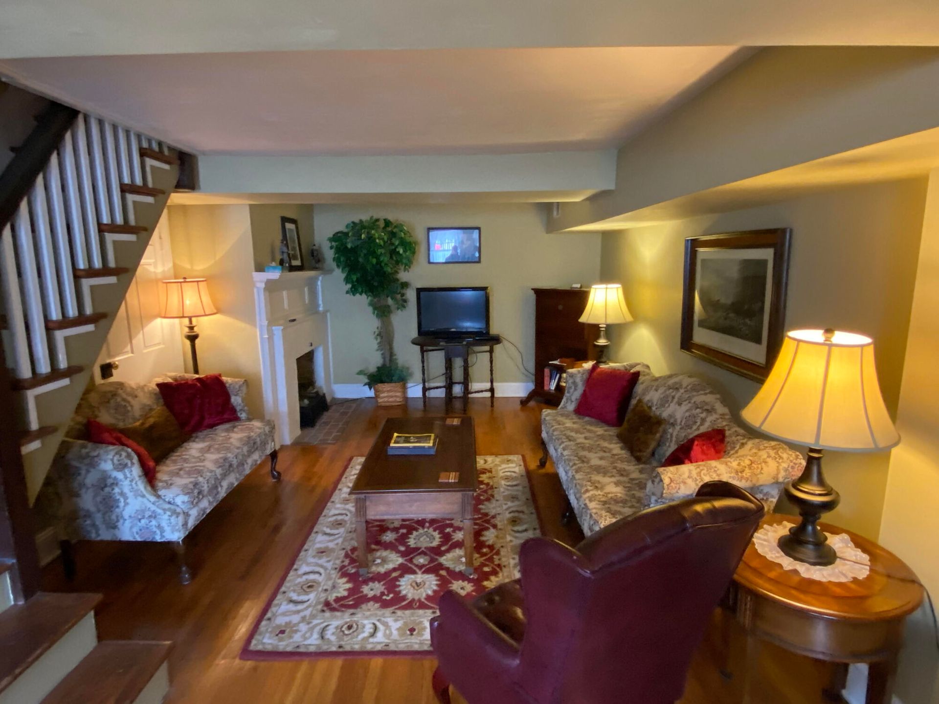 Cozy living room with floral sofas, wooden coffee table, lamps, rug, and TV against a beige wall.