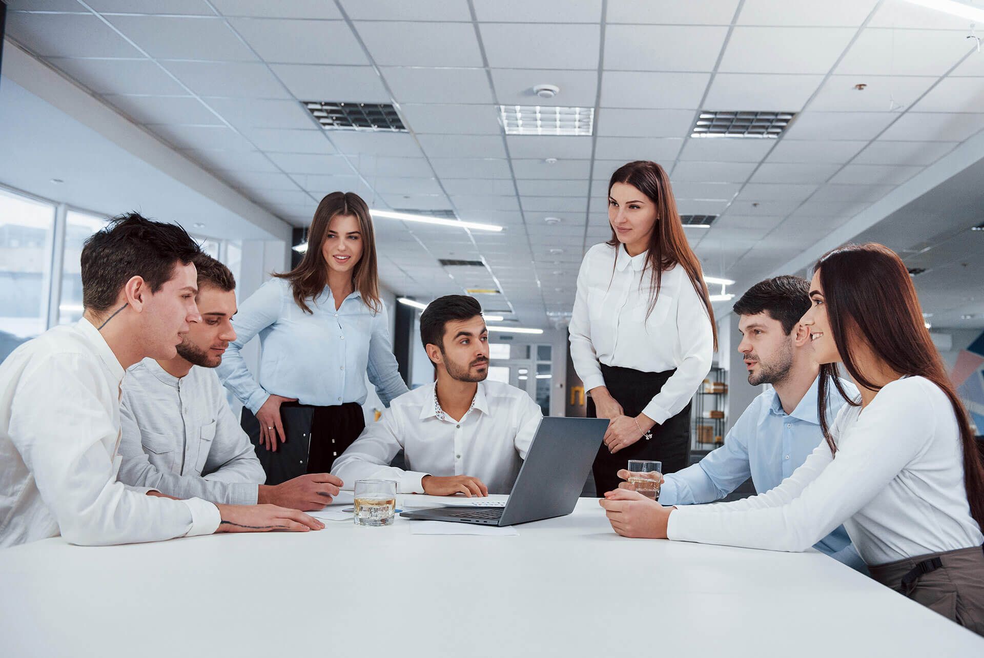 Un grupo diverso de profesionales vestidos de traje colabora alrededor de una mesa blanca en una oficina luminosa y moderna.