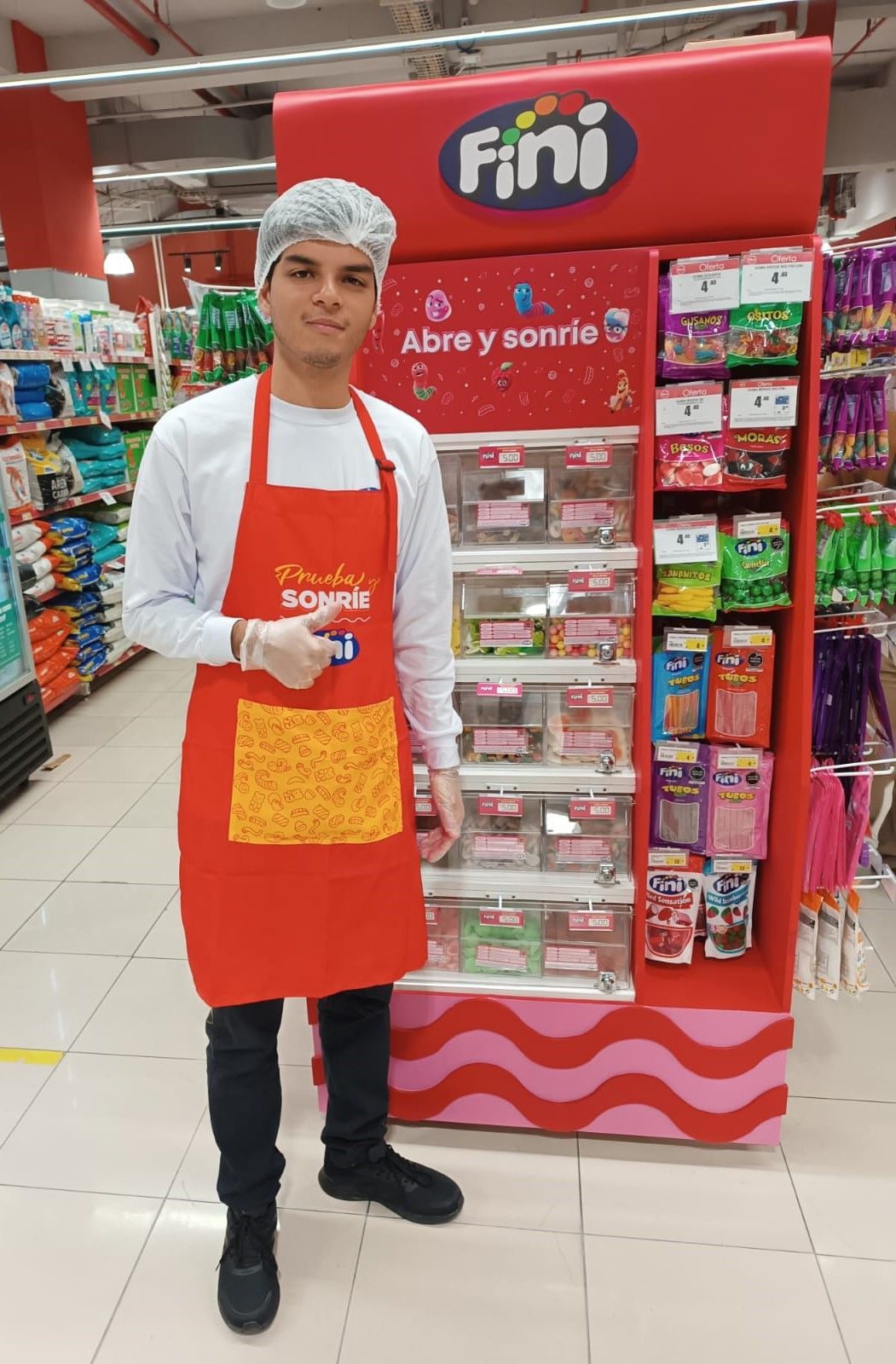 Una trabajadora con redecilla para el pelo y delantal rojo de la marca Fini levanta el pulgar