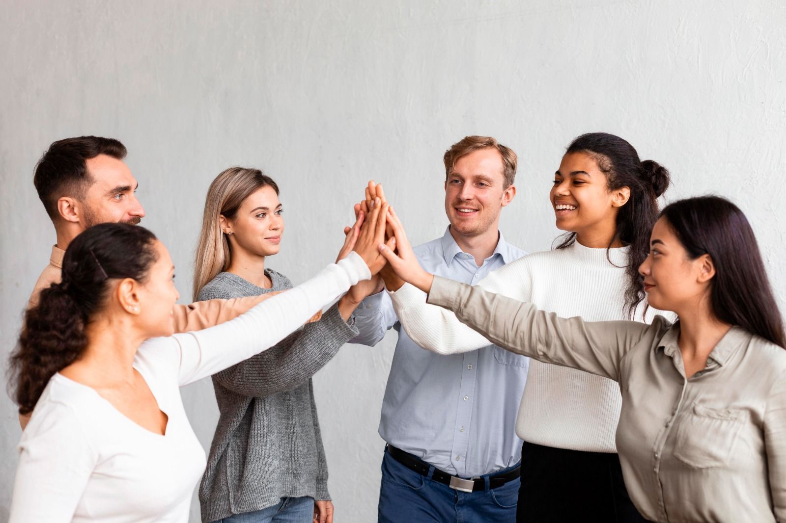 Un grupo diverso de seis personas de pie en círculo, sonriendo y juntando las manos en un gesto de saludo con las palmas.