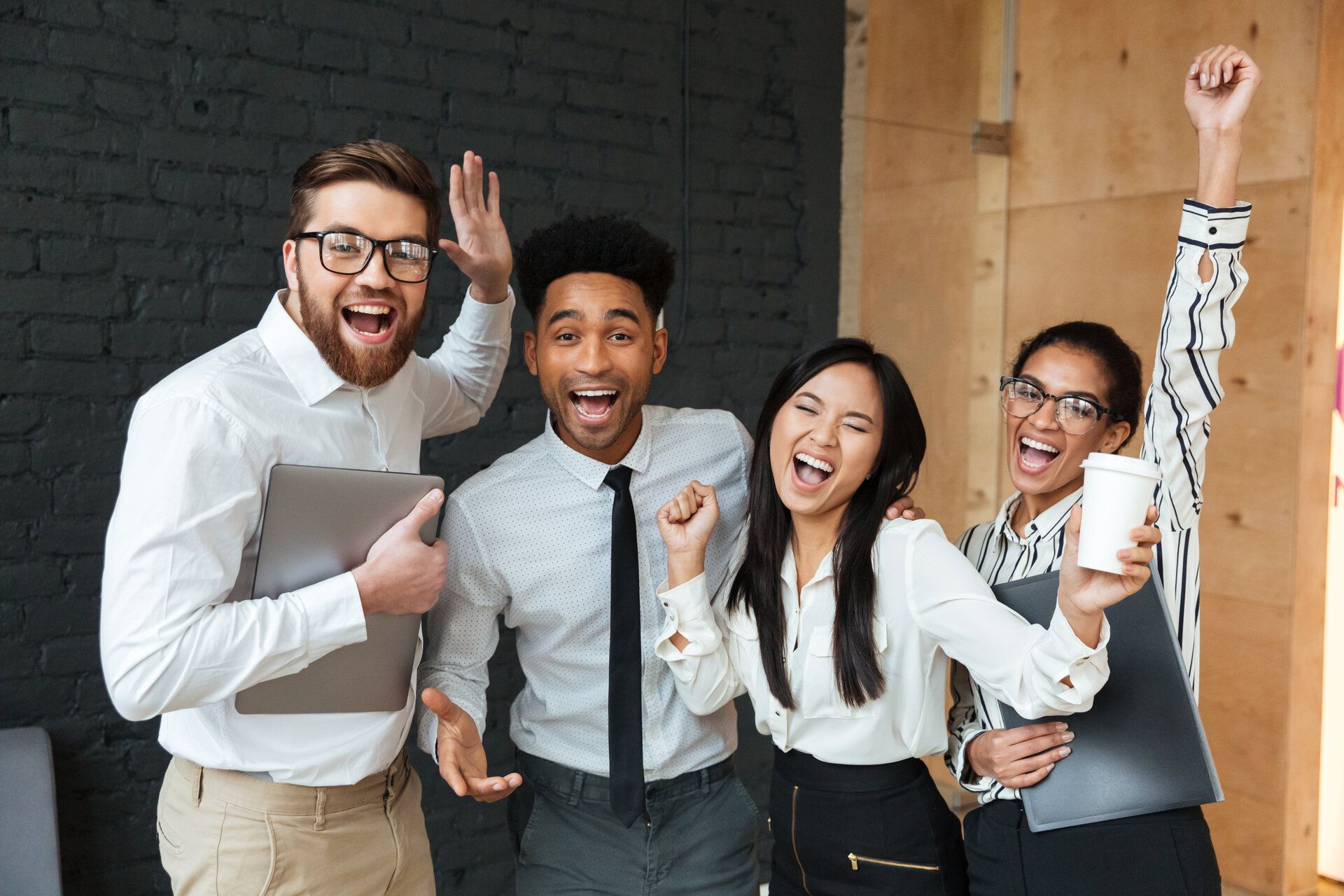 Cuatro compañeros de trabajo celebran en una oficina con expresiones de alegría