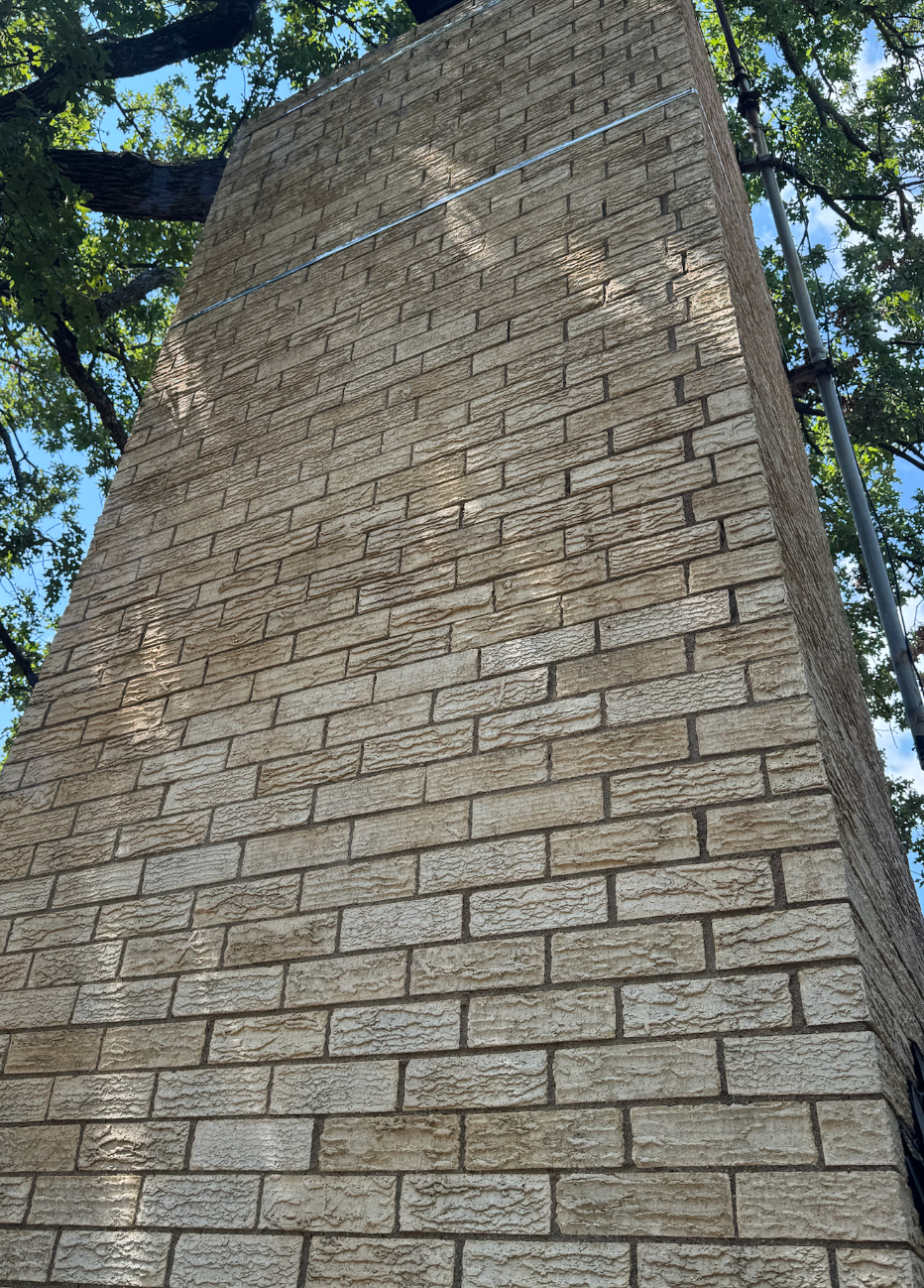A tall brick chimney on a house with trees in the background.
