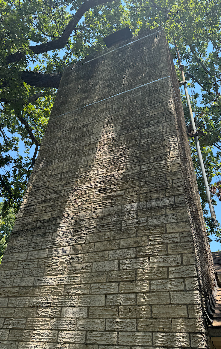 A large brick chimney on a house with trees in the background.