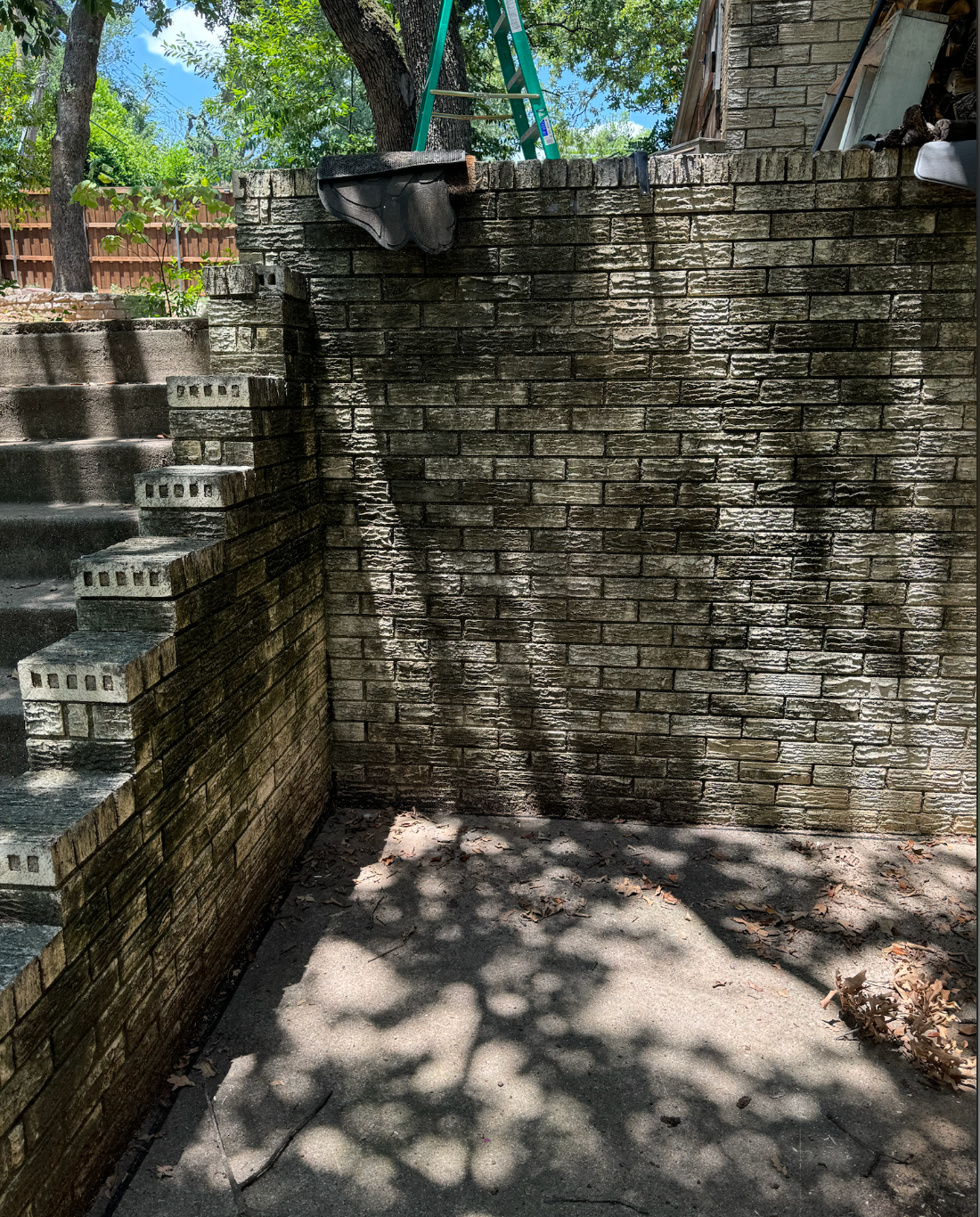 A brick wall with stairs leading up to it and trees in the background.