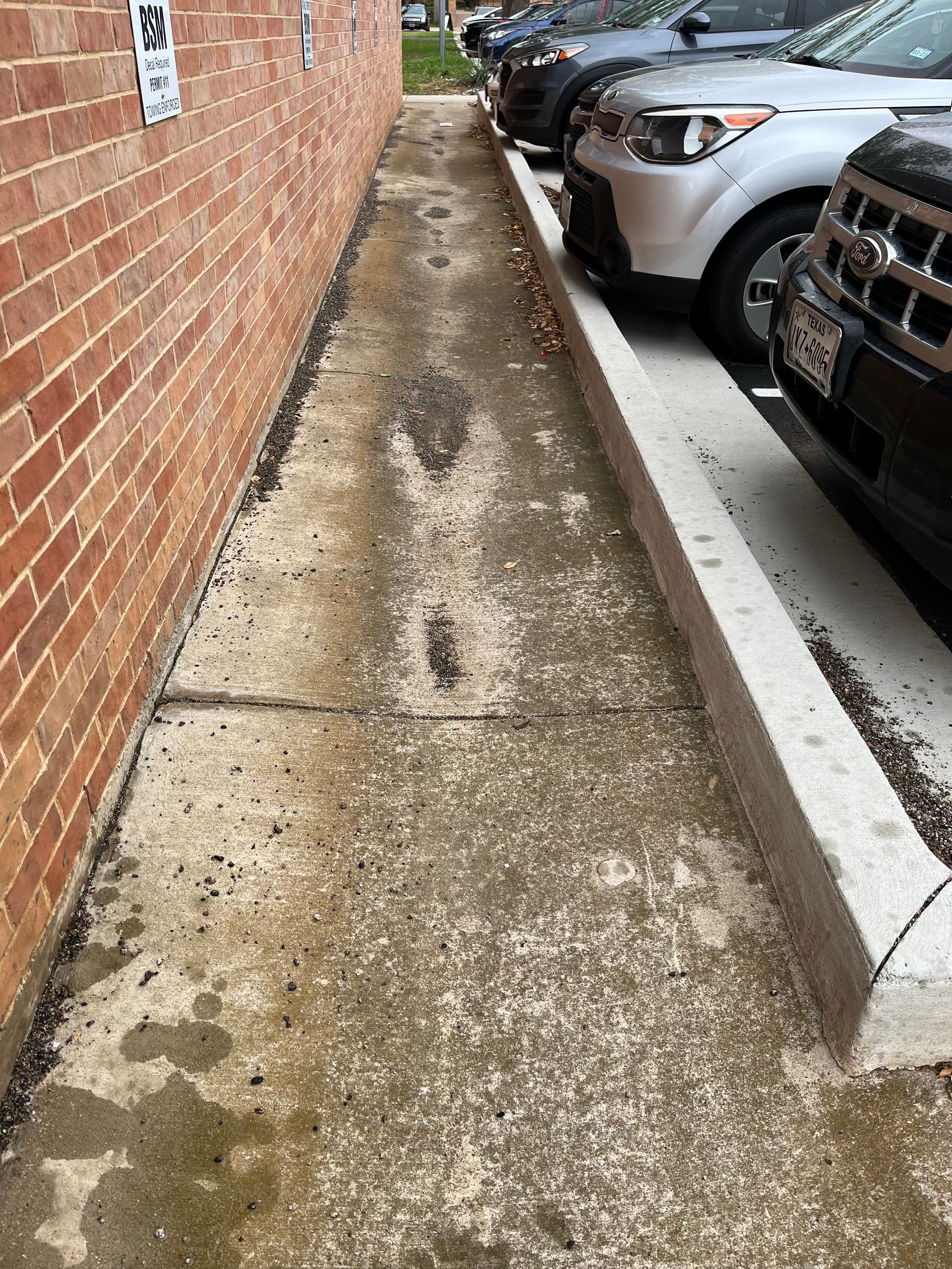 A row of cars are parked in a parking lot next to a brick building.