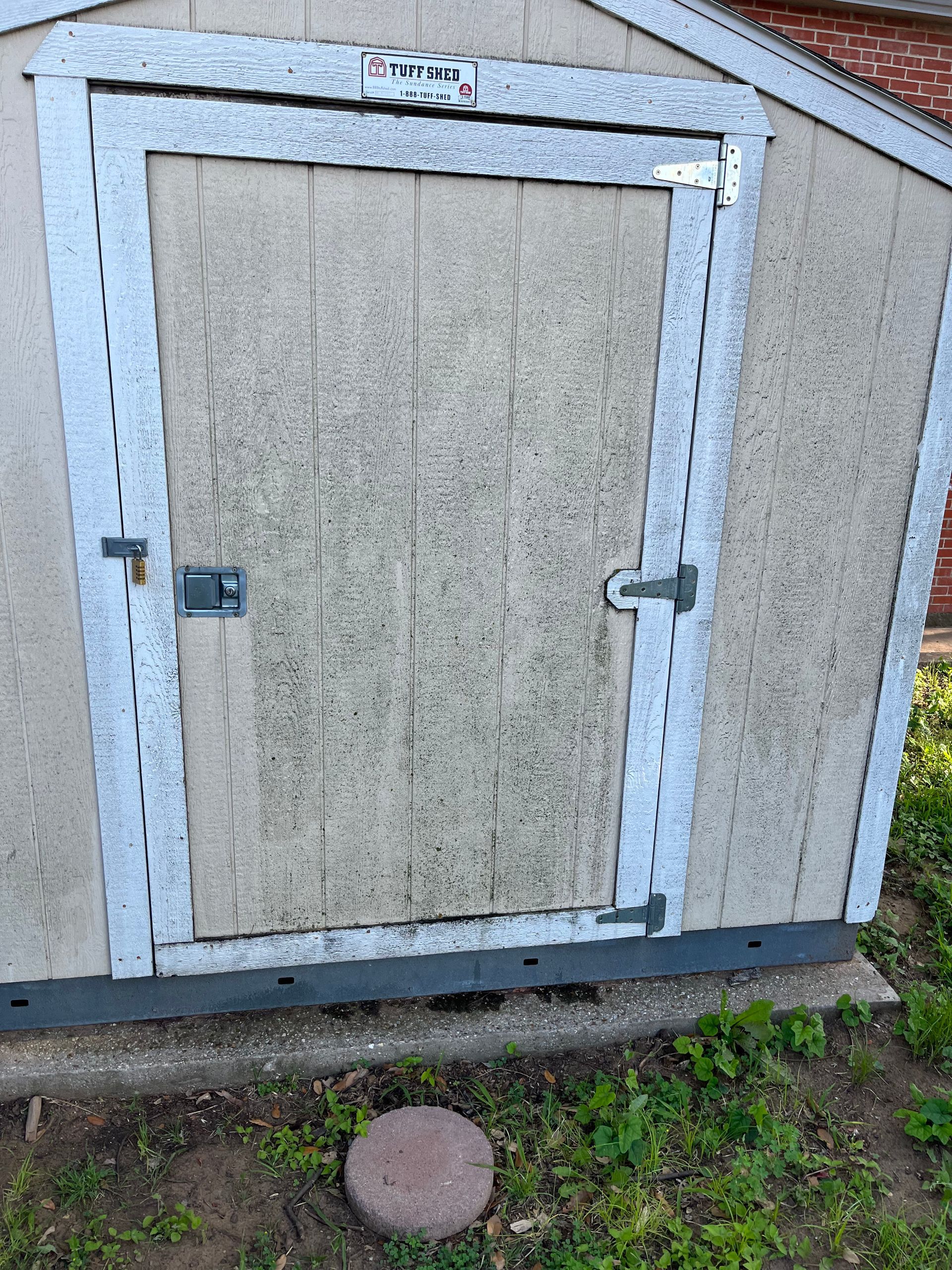 A small shed with a door is sitting in the grass.