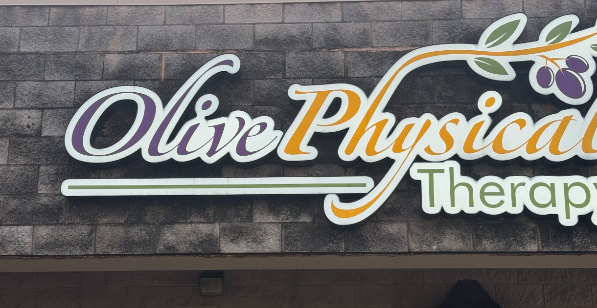 A sign for olive physical therapy is on a brick wall.