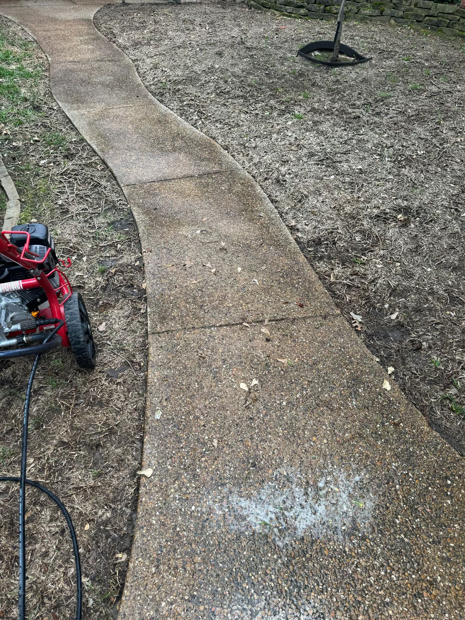 A person is using a pressure washer to clean a concrete walkway.