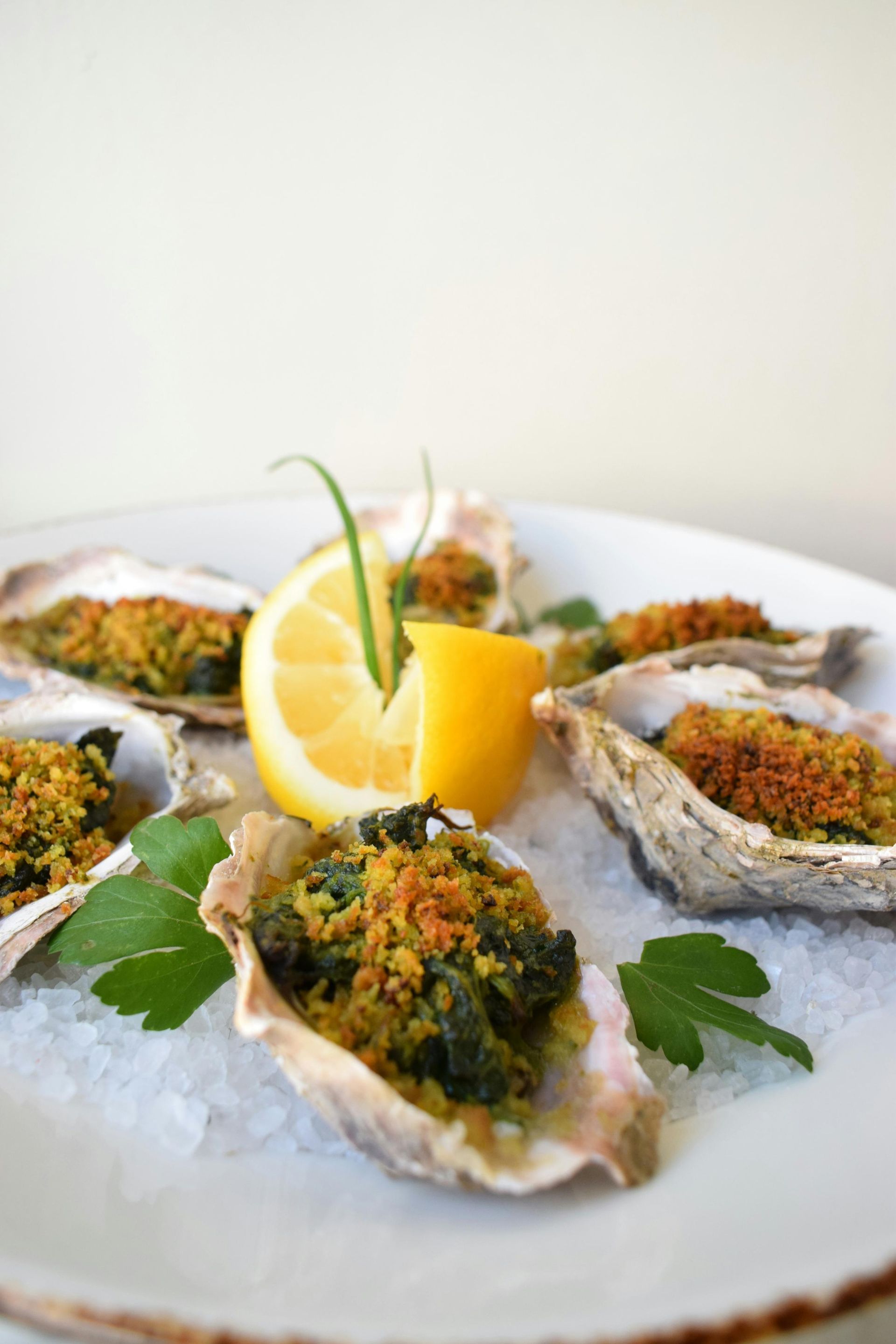 A plate of Oysters Rockefeller on a bed of crushed ice, garnished with a lemon wedge and fresh parsley.