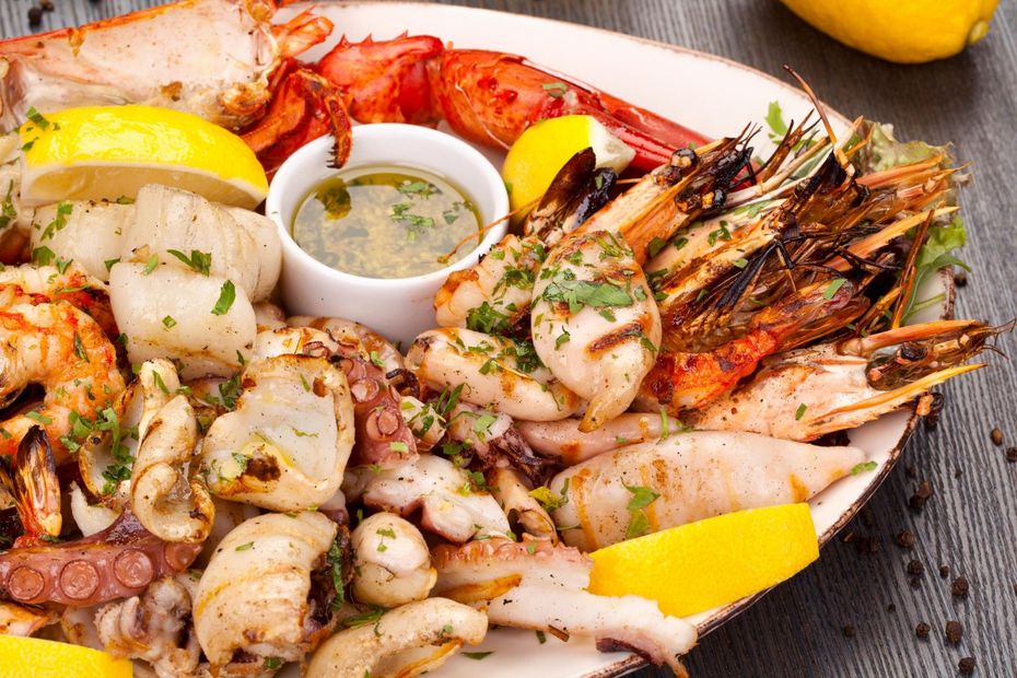 A platter of grilled seafood including lobster, shrimp, octopus, and scallops, garnished with herbs and lemon wedges.