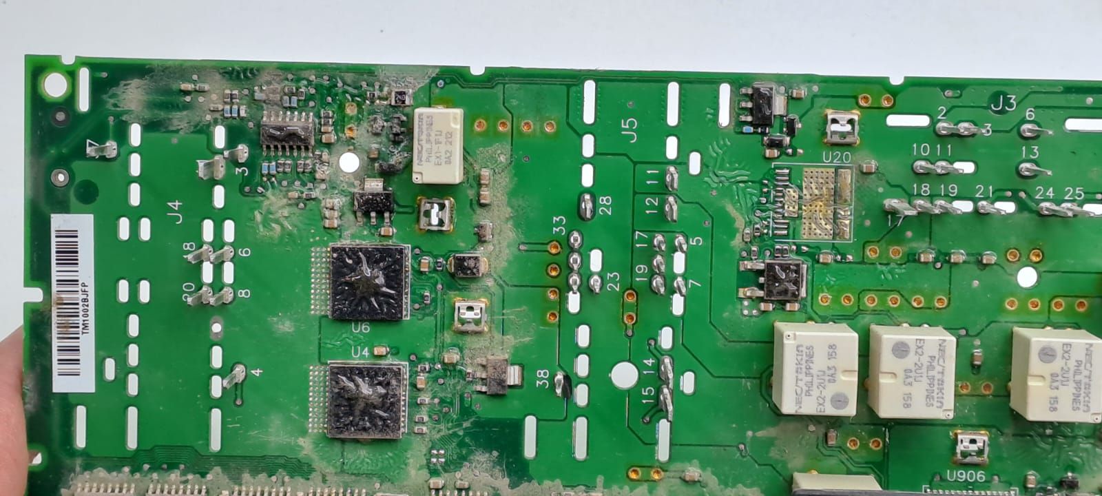 Placa de circuito impreso verde con componentes electrónicos, chips, relés y conectores.