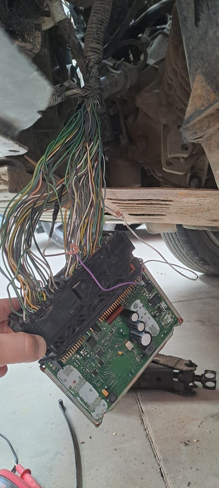 Placa de circuito dañada con cables multicolores enredados colgando del techo y una mano sosteniéndola.