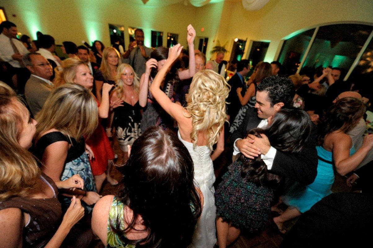 Crowded dance floor at a lively party, with people dancing under warm lights and raised arms.