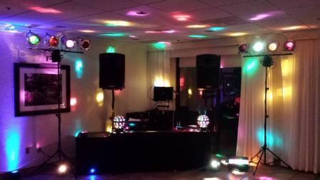 DJ booth with colorful disco lights in a dark room, speakers and cables on a stage setup