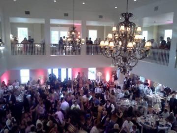 Crowded ballroom reception with tables, guests, and chandeliers in a two-story venue