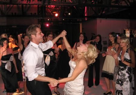 Couple dancing in a dimly lit party room, surrounded by guests watching and clapping.