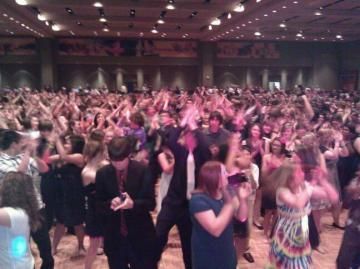 Crowded ballroom with people dancing and raising their hands under warm ceiling lights