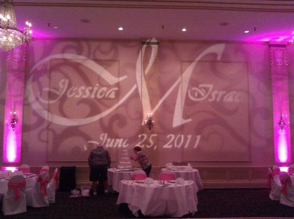 Pink-lit banquet hall with wedding backdrop reading “Jessica” and “Isa” and date “June 25, 2011”