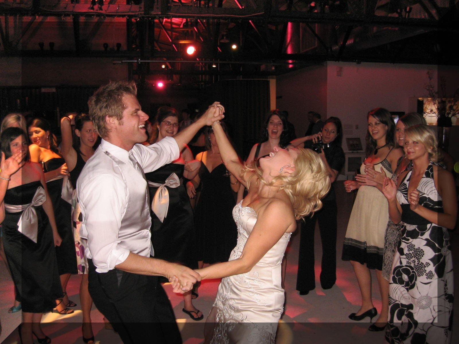 Couple dancing at a party, with other guests watching in a dimly lit room.