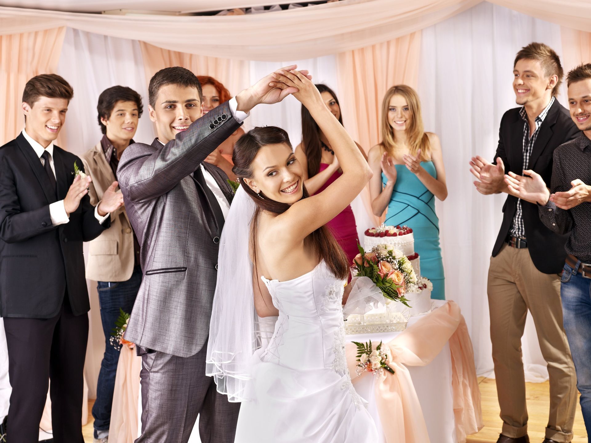 Bride and groom dancing at a wedding reception while guests applaud nearby