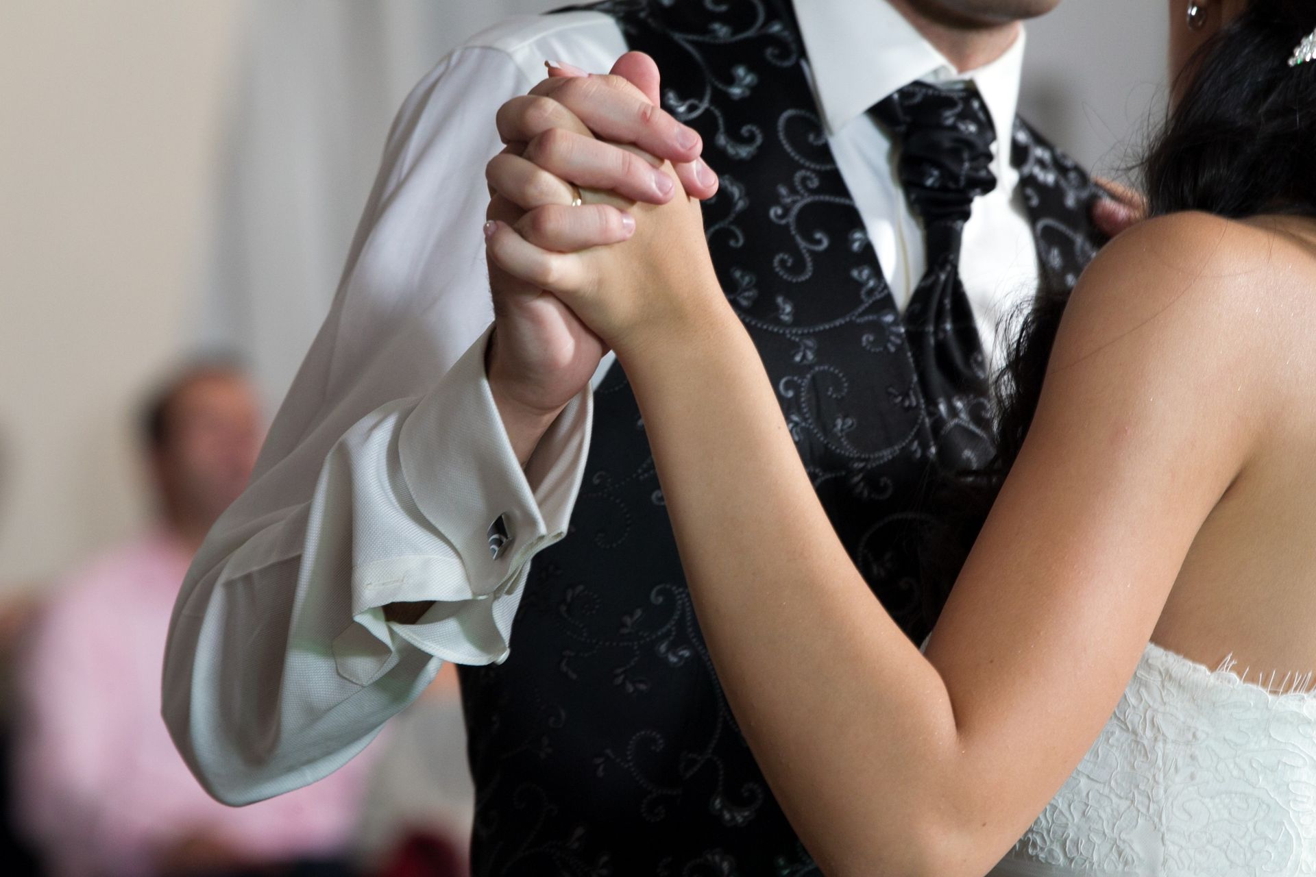 Couple dancing, holding hands, with a white dress and black vest in a formal setting
