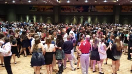 Crowded dance floor in a large hall, with people in casual clothes socializing and dancing under warm lights