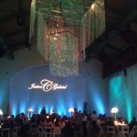 Indoor banquet hall with blue uplighting, chandelier, and guests seated at tables near a lit stage