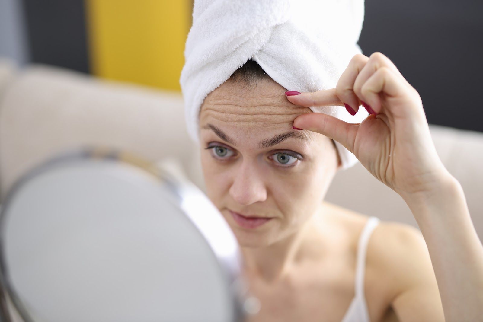 Person with a towel on their head checking skin in a mirror