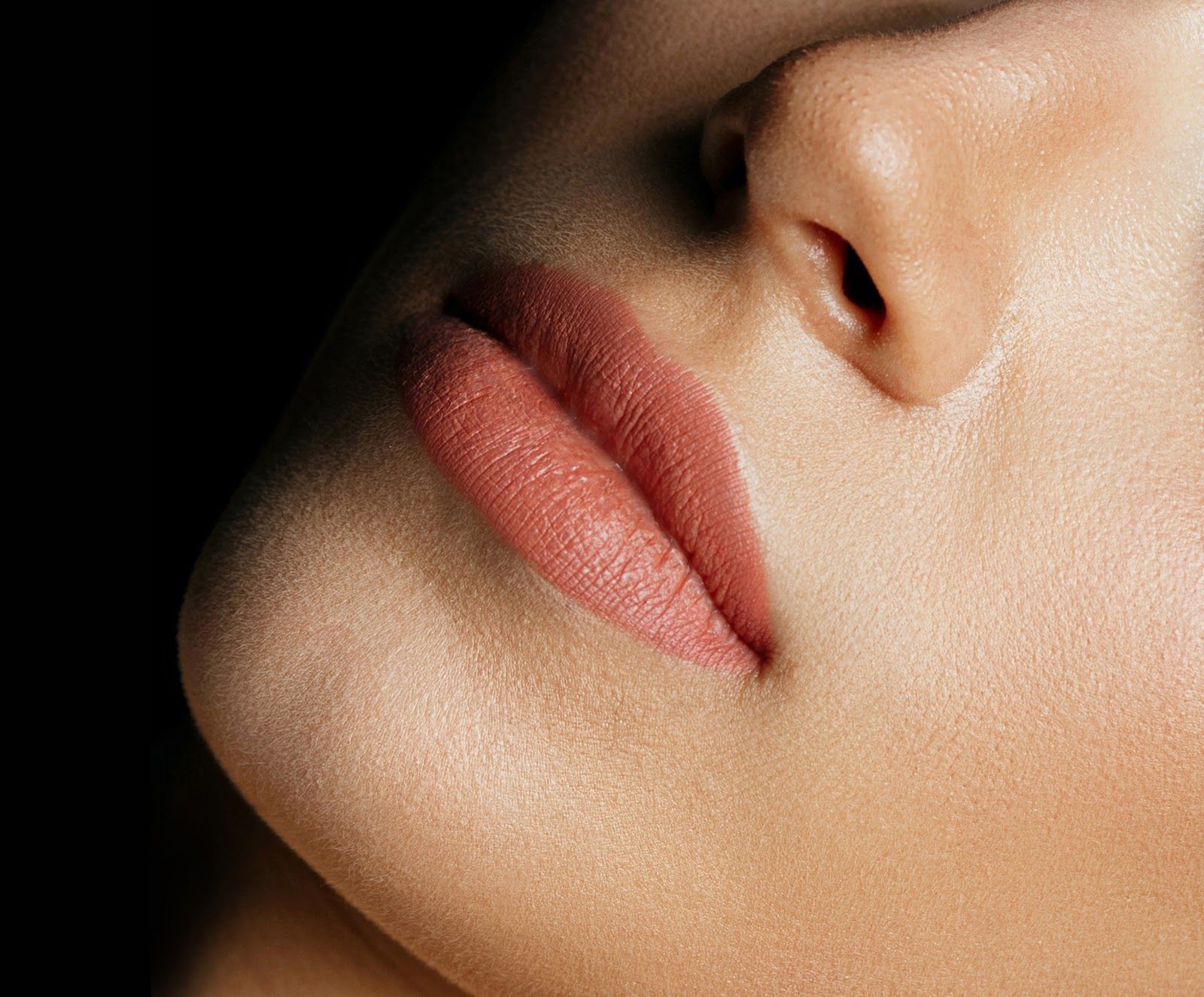 Close-up of a face showing pink lips and a nose against a dark background