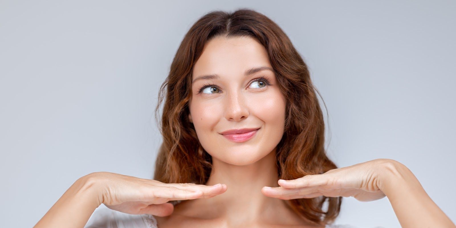 Smiling woman with hands under chin, looking upward against a light gray background
