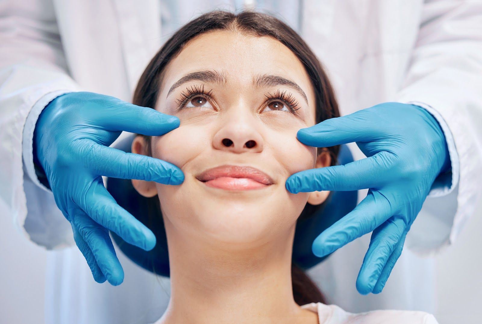 Gloved hands gently examine a woman’s face in a clinical setting