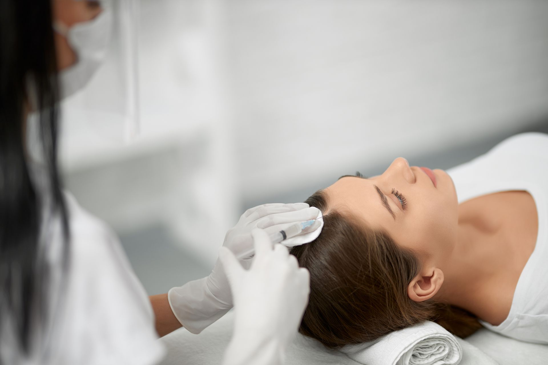Cosmetician applying treatment to a woman’s face while she lies on a spa bed