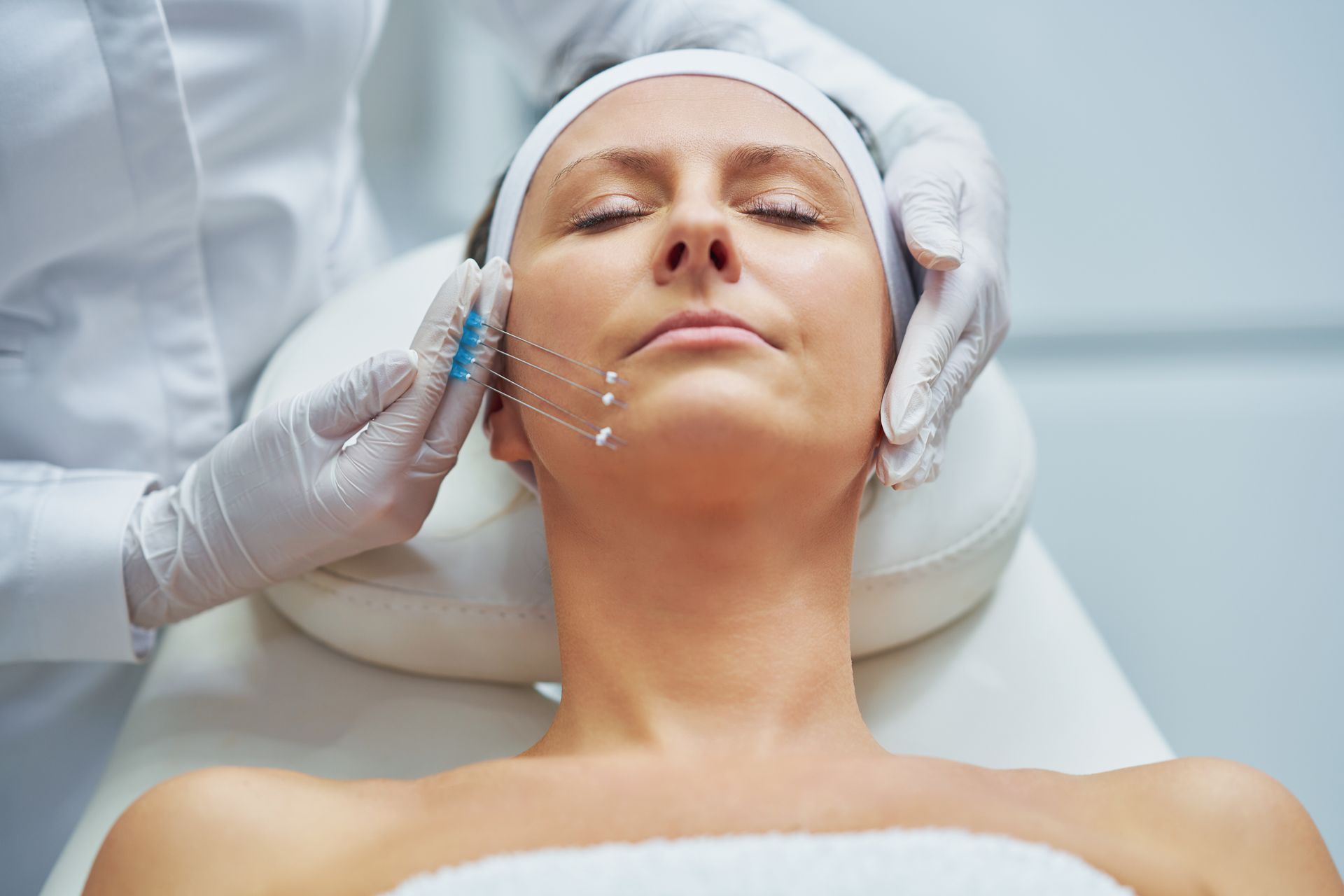 Woman receiving a facial treatment while lying on a spa table, with gloved hands applying product to her cheek.