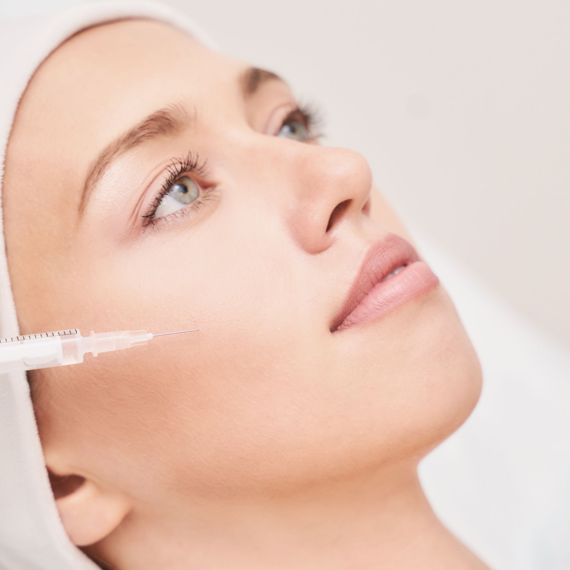 Woman receiving a facial injection. She has fair skin, light eyes, and is lying down with a medical professional nearby.