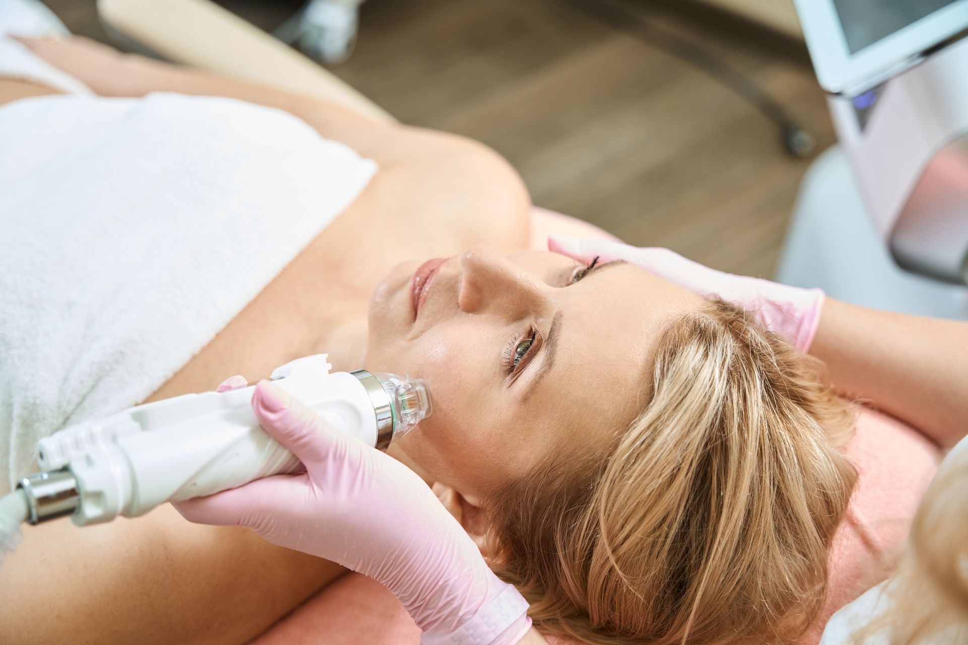 Facial treatment with gloved hands using a handheld device on a reclining client