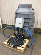 Industrial pump and hoses on a wooden pallet in front of a large gray tank outdoors