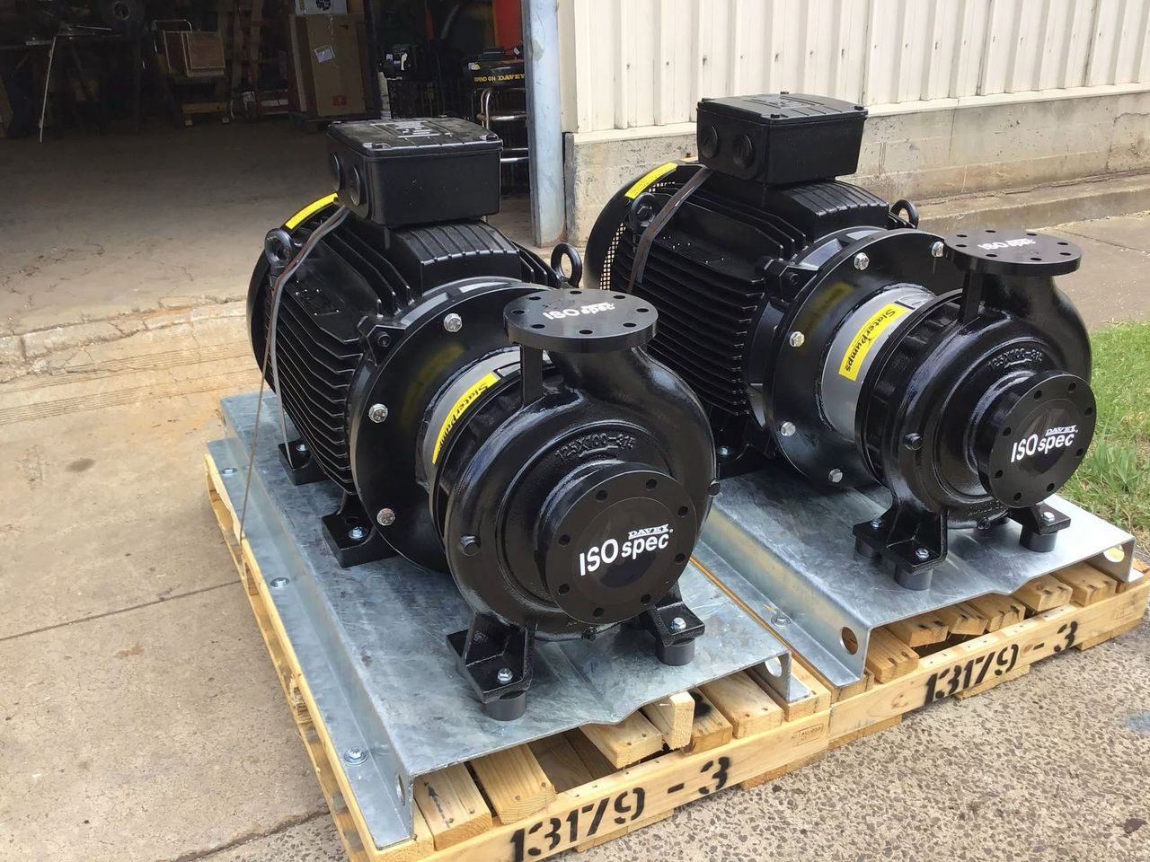 Two black industrial motors on wooden pallets outside a warehouse