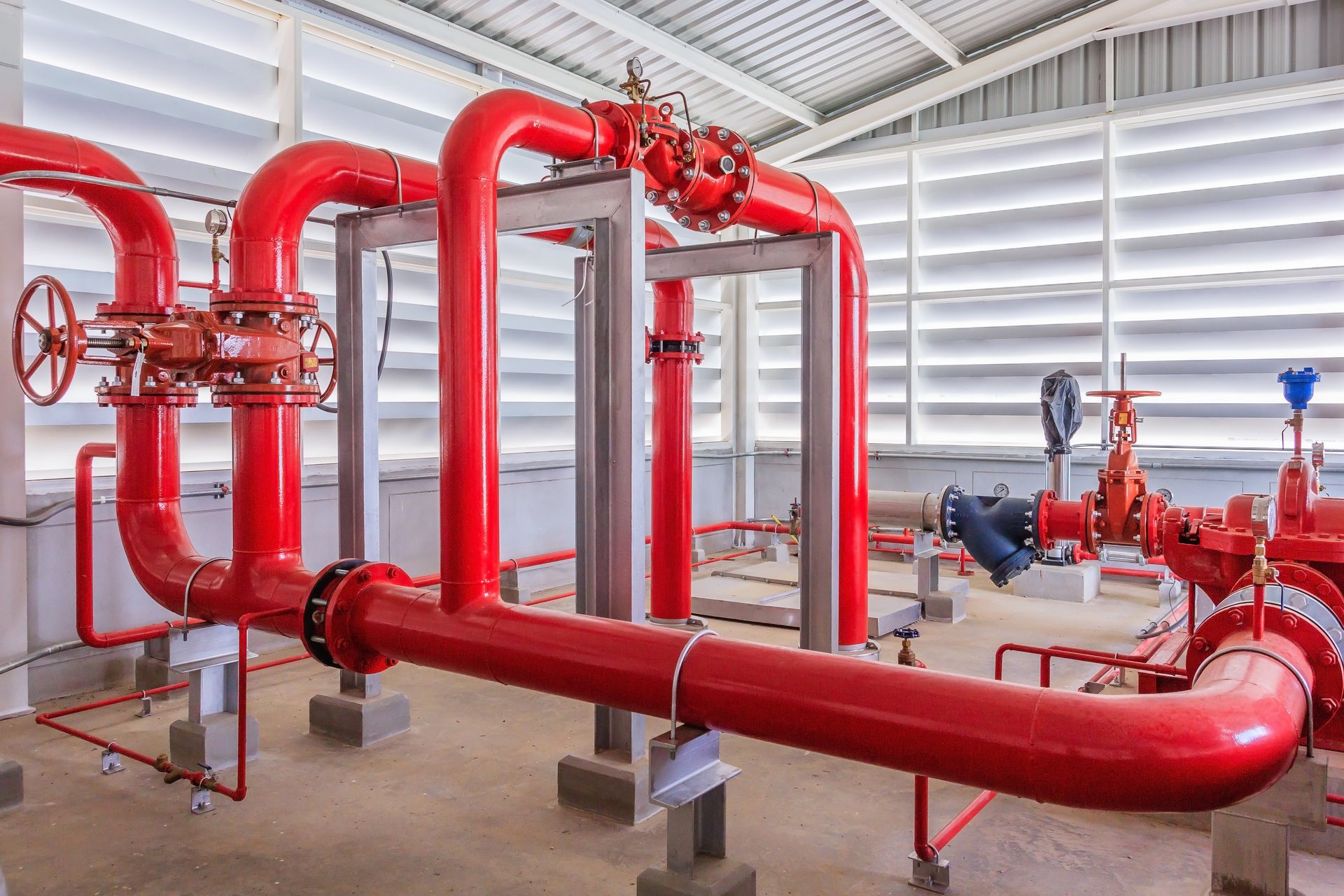 Red industrial pipes and valves in a utility room with white ceiling beams.