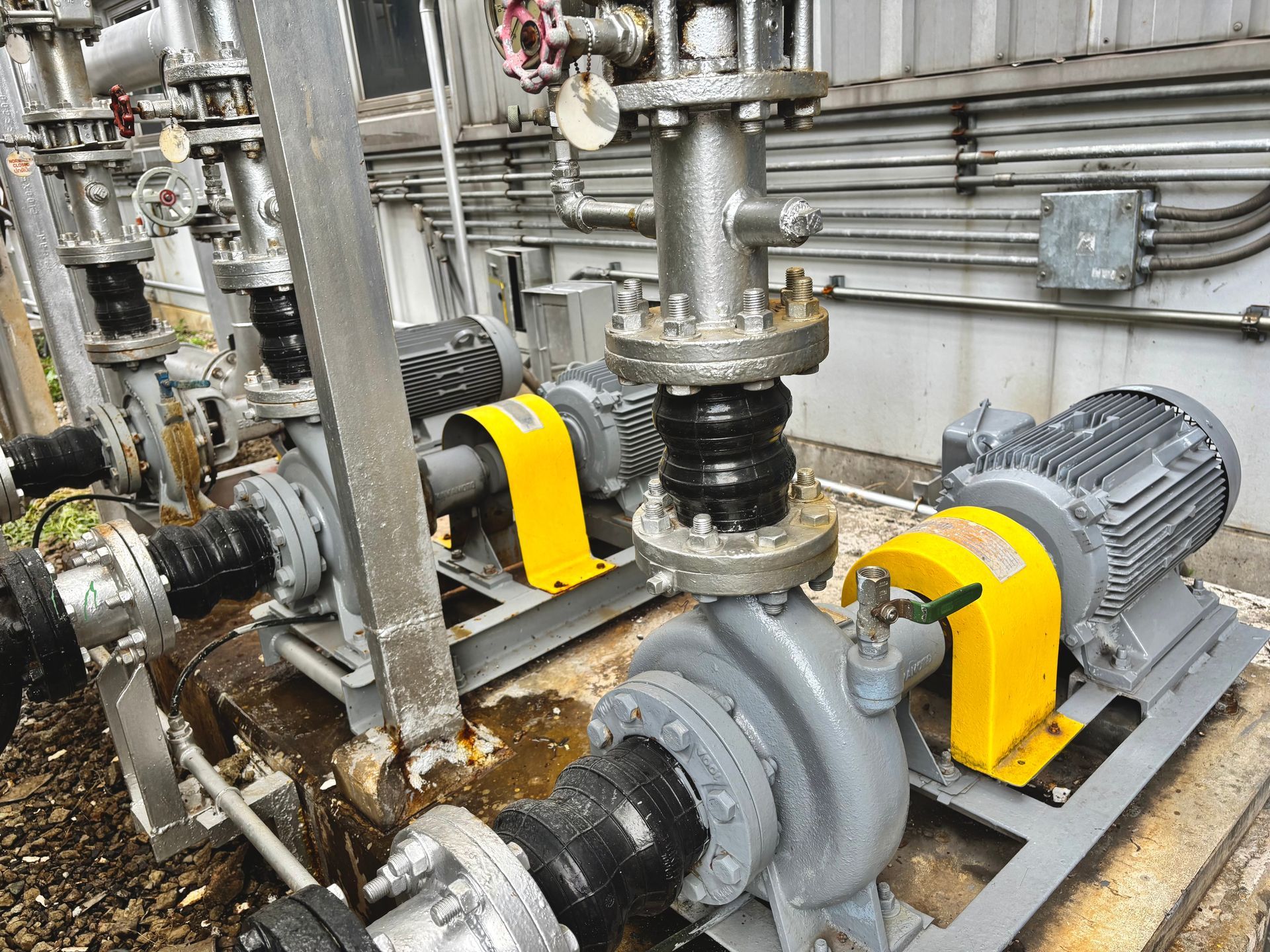 Industrial pumps and pipes in a mechanical room, with gray motors and yellow safety guards.