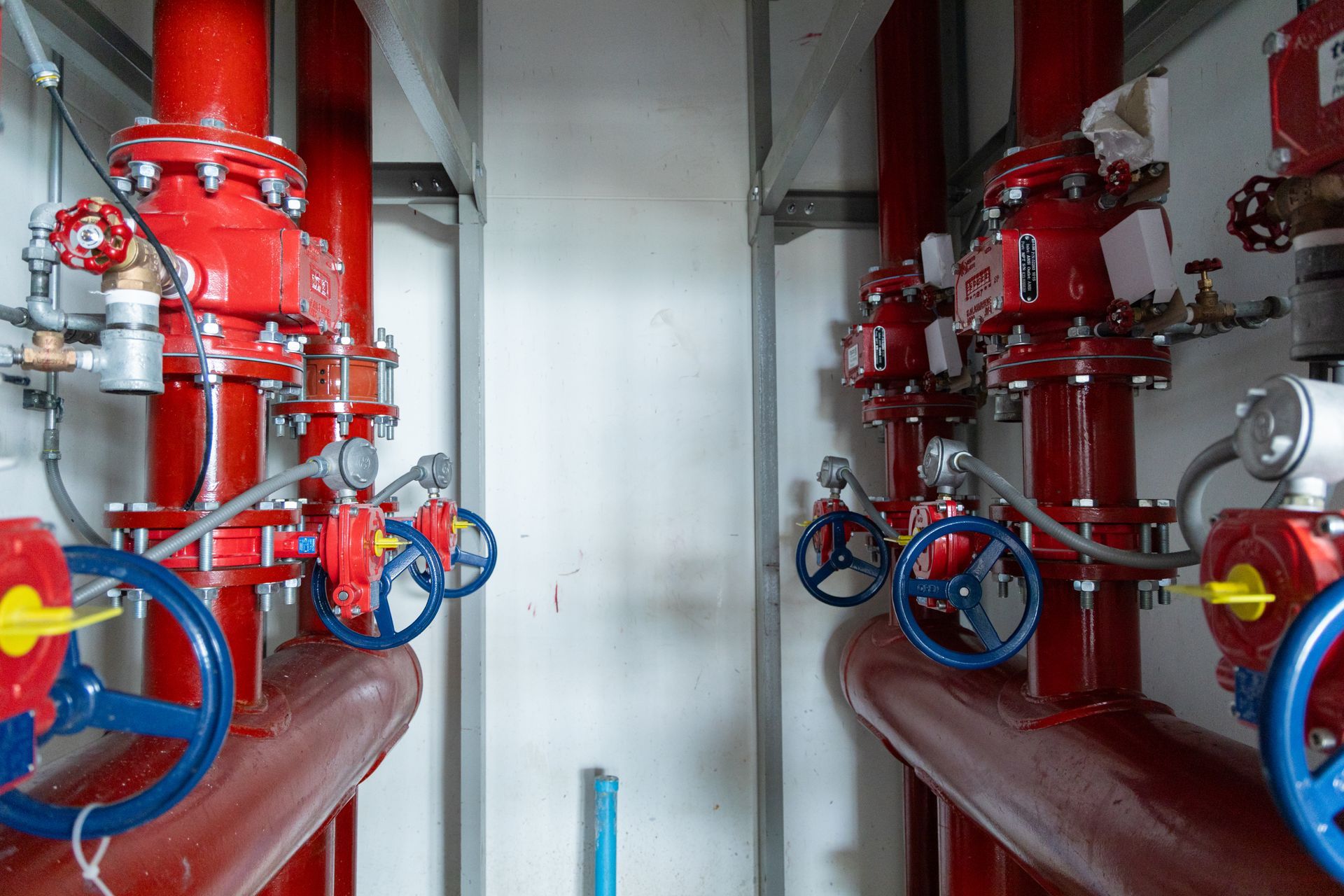 Red industrial pipes and blue valves in a mechanical room, viewed down a narrow corridor