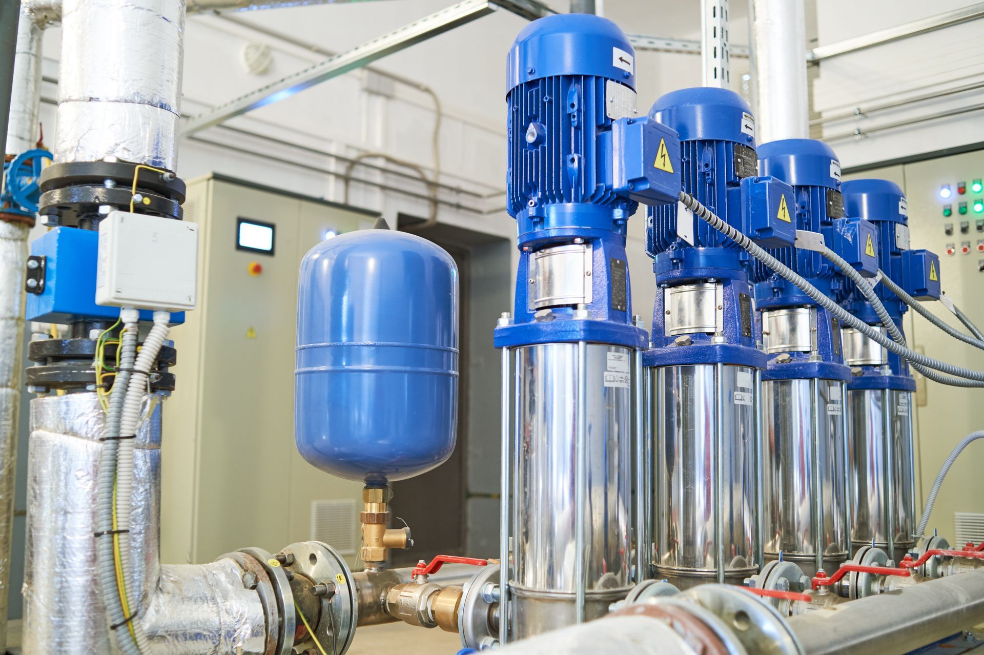 Blue industrial pumps and tanks in a machinery room with metal pipes and gauges