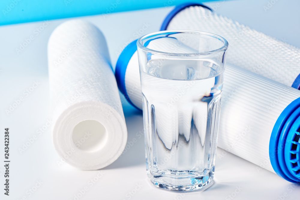Glass of water with white pills and blue-and-white rolled towels on a white background