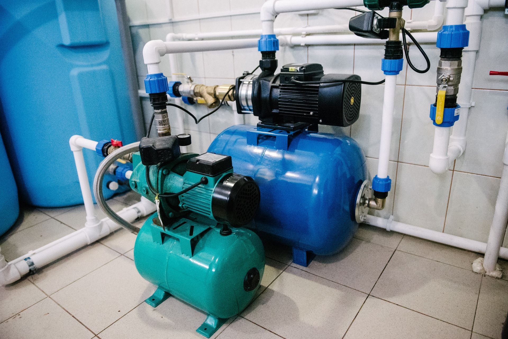 Blue and green water pumps with pipes in a tiled utility room