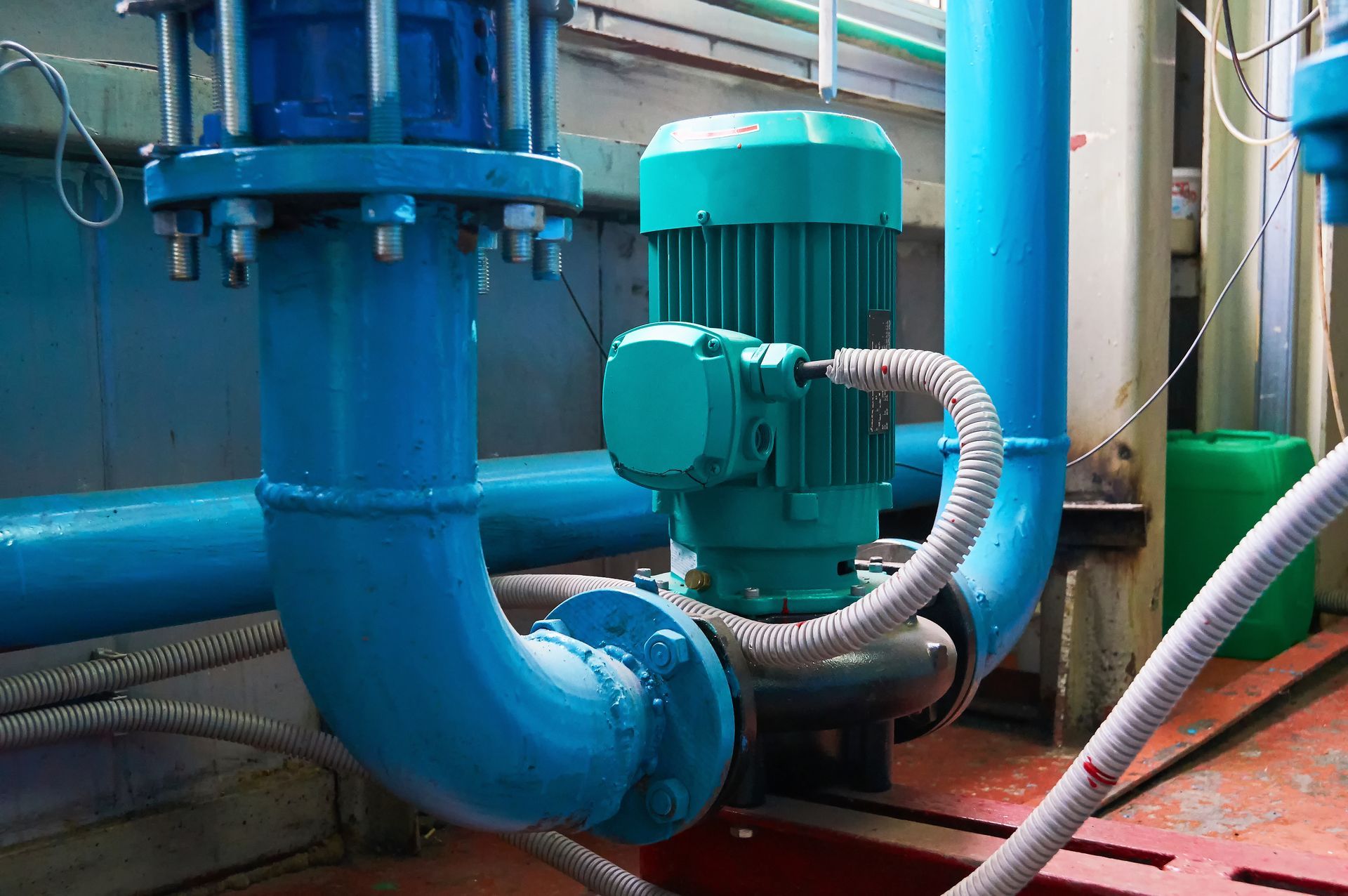 Blue industrial pipes and a green motor in a utility room with hoses and valves