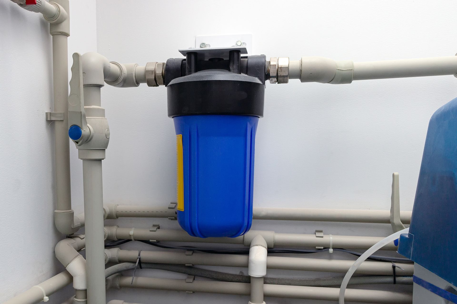 Blue water filter housing with gray pipes in a utility room