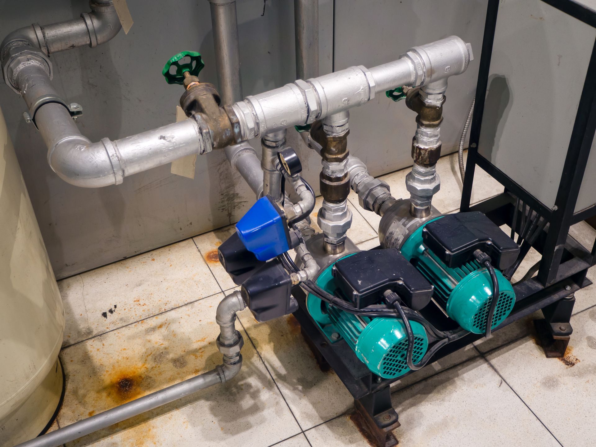 Industrial pump and pipe system with teal motors, silver piping, and a blue valve in a utility room