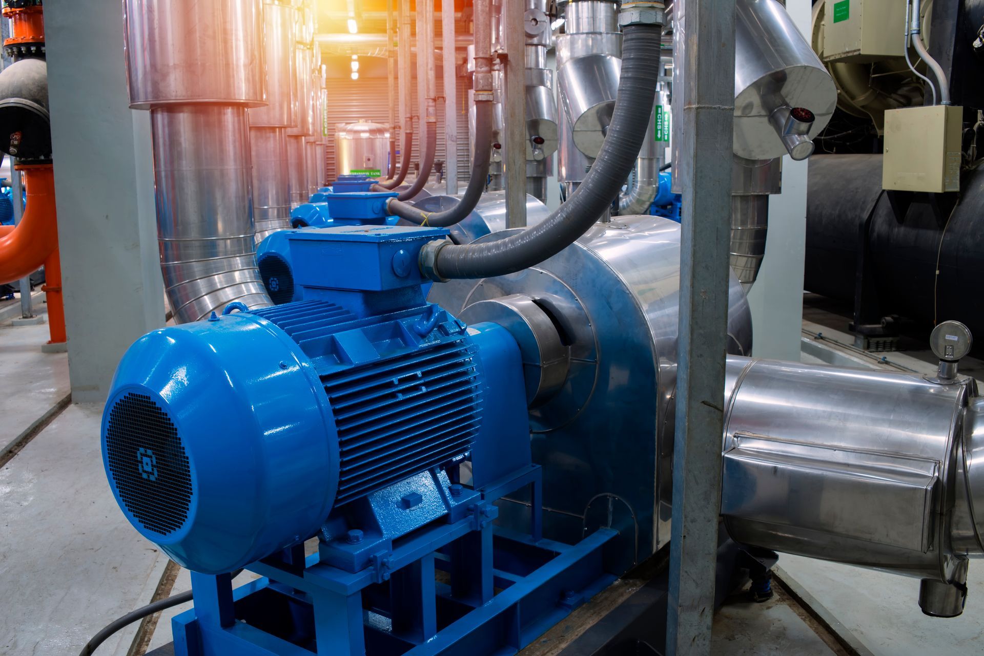 Blue industrial motor and pump connected to stainless steel pipes in a factory setting